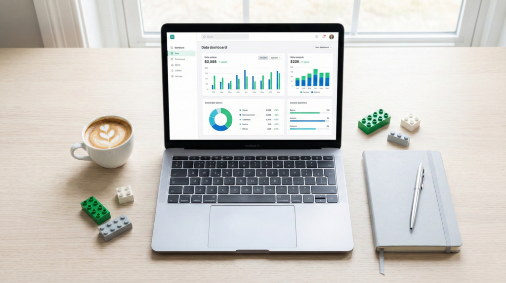 Visão superior de um ambiente de trabalho moderno e organizado, com um notebook exibindo um painel de dados colorido na tela. Ao lado, há uma xícara de café, um caderno e algumas peças de LEGO soltas, simbolizando a construção de conhecimento e análise lógica.